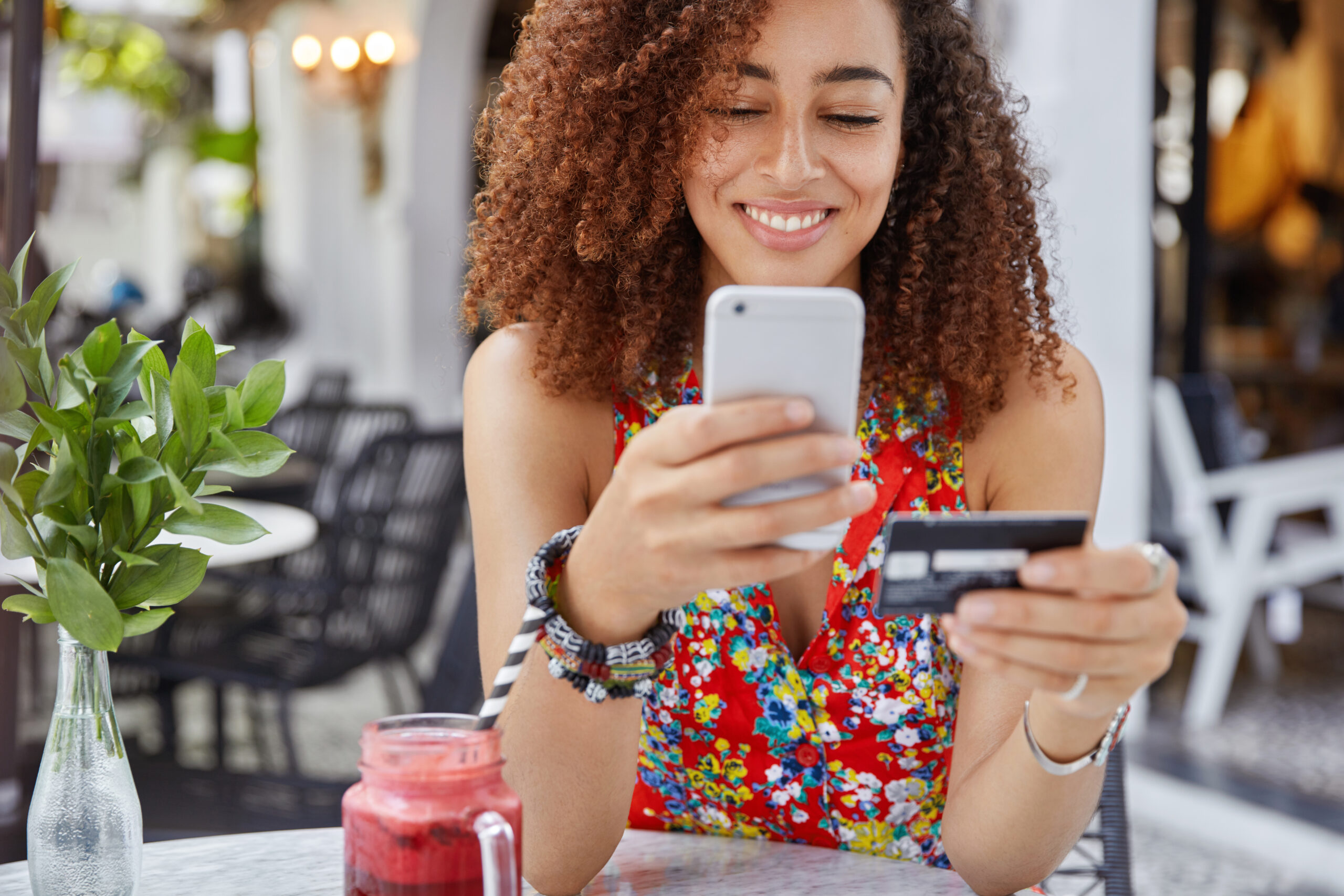 Mulher lendo sobre o que é tráfego pago no celular e com um cartão de crédito na outra mão.